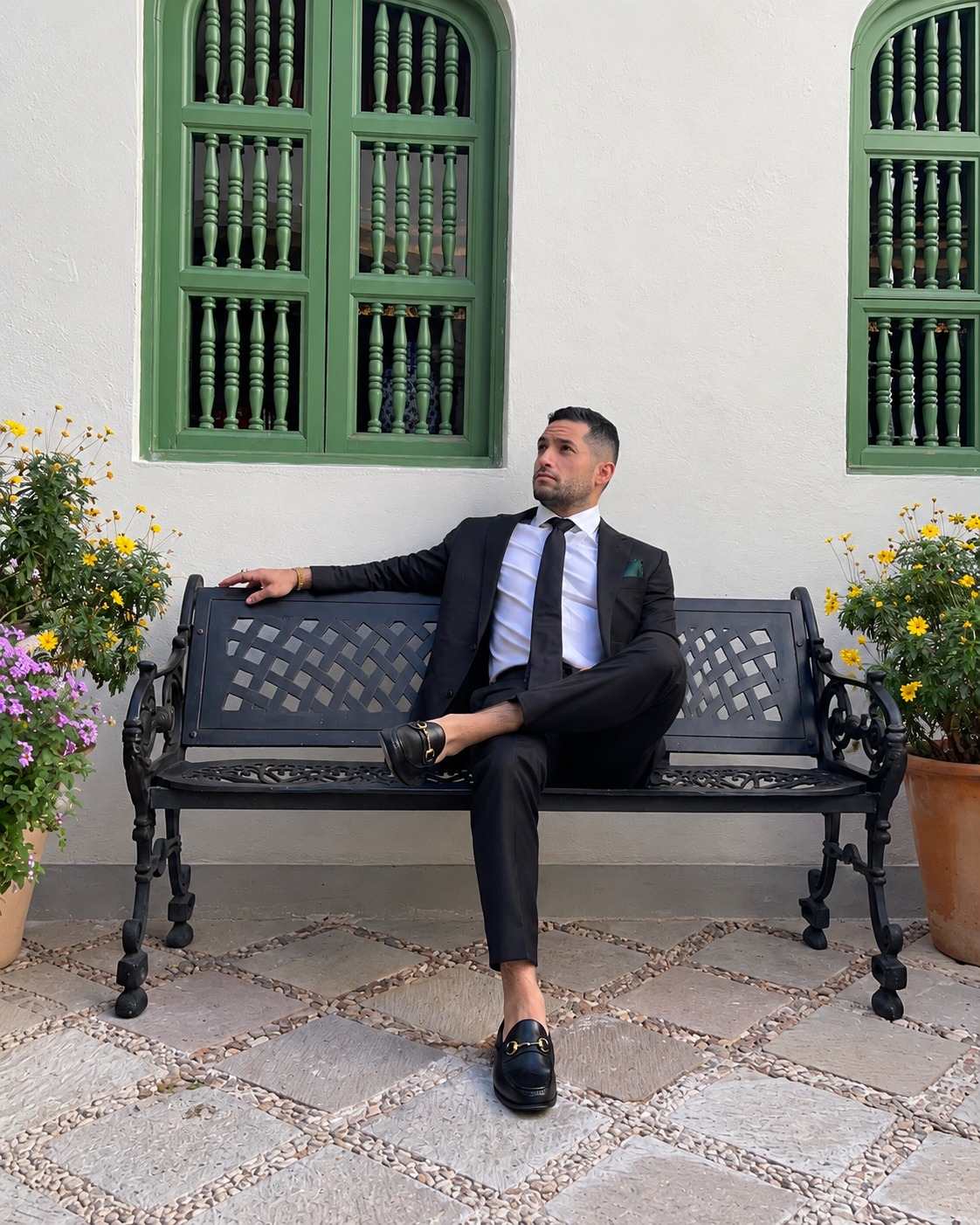 Eric Escobar seated on a bench in a dark suit beside green shutters.